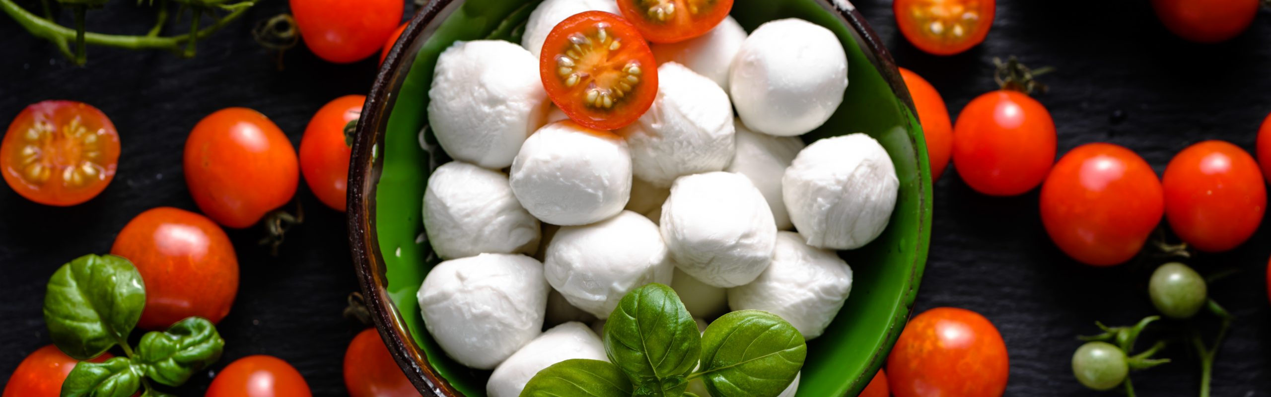 Italian food background. Mozzarella, tomatoes, and basil on dark slate, overhead