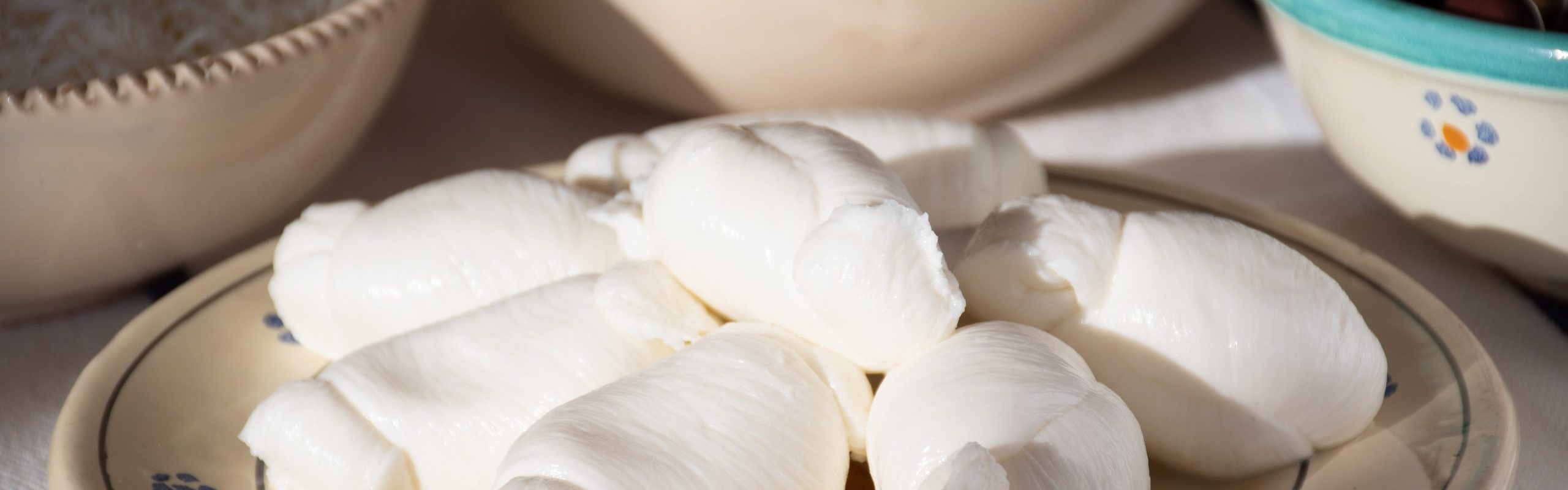 Fresh Mozzarella, traditionally southern Italian cheese made from Italian milk by the pasta filata method in a traditional terracotta plate with taralli, cheese and olives on background